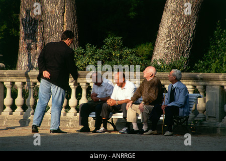 Eine Gruppe von älteren Herren entspannen im Schatten einiger der alte Baumbestand auf dem Gelände der Palau Reial de Pedralbes beherbergt das Museu de Ceramica-Barcelona Stockfoto