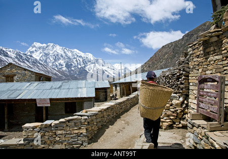 Mann mit traditionellen Korb. Auf dem Hintergrund der Annapurna III (7555m). Ghyaru Dorf. Annapurna Circuit Trek. Nepal Stockfoto