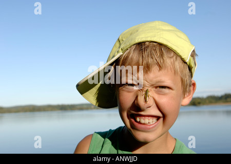 Junge, elf Jahre alte, mit einer Heuschrecke auf der Nase Stockfoto