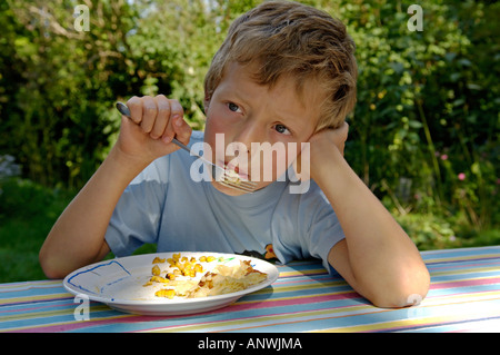 Junge, neun-jährige. ist verträumt sein Essen mit Mais Stockfoto