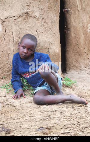 Maasai Boy außerhalb Lehmhütte gemacht von Stöcken und Kuhmist Masai Mara National Nature Reserve Kenia in Ostafrika Stockfoto