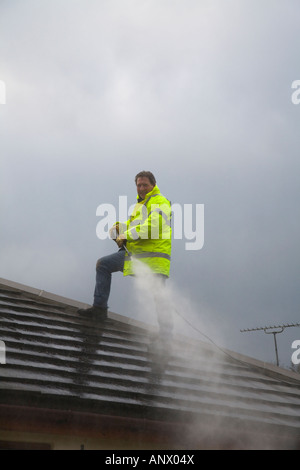 Ein Mann, der das Dach eines Hauses mit einem Hochdruckwasserstrahl Reinigung spray Hochdruckreiniger. Haus von außen. VEREINIGTES KÖNIGREICH. Stockfoto