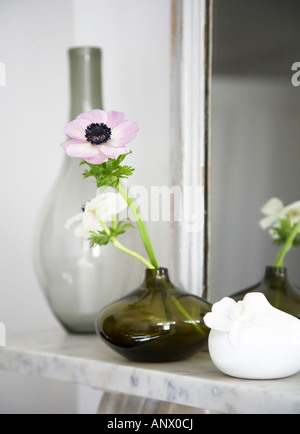 2 Mohn in einer grünen Glas Vase auf einem Marmor Kaminsims als nächstes eine gerahmte Spiegel, eine weiße Porzellanvase und grau Glasvase Stockfoto