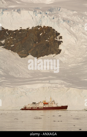 Eine Expedition Kreuzfahrtschiff ist durch die Gletscher in den Schatten gestellt, die es neben dem in Neko Harbor auf der antarktischen Halbinsel verankert ist Stockfoto