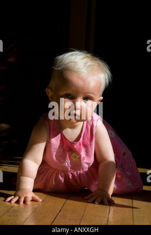 Stock Foto von einem 1 Jahr alten Baby Mädchen kriecht entlang einen Holzboden in einem rosa Kleid Stockfoto