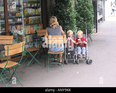 zwei jungen im Kinderwagen sitzen im Twin Kinderwagen aus Karton Becher vor Restaurant mit ihrer Mutter zu trinken Stockfoto