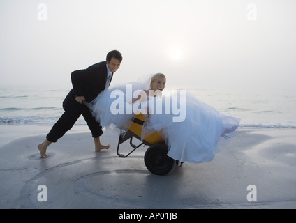 Bräutigam, die Braut in Schubkarre schieben, am Strand Stockfoto