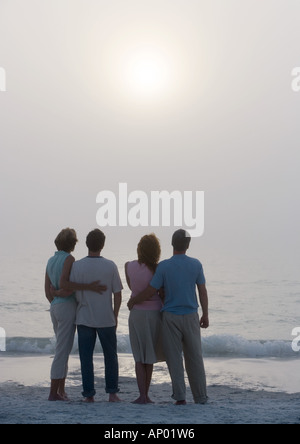 Zwei Paare stehen am Strand in der Abenddämmerung, Rückansicht Stockfoto
