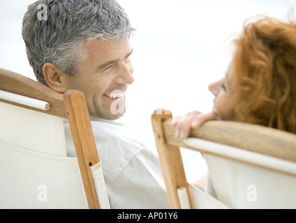 Älteres Paar, sitzen in Liegestühlen, Lächeln einander an Stockfoto