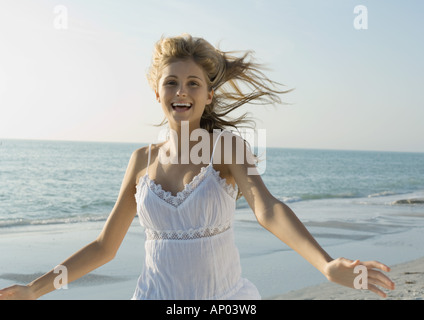 Junge Frau läuft mit Armen draußen am Strand Stockfoto