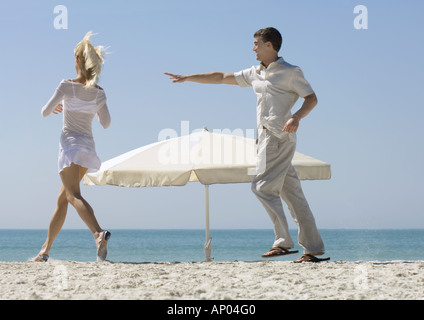 Paar jagen einander um Sonnenschirm am Strand Stockfoto