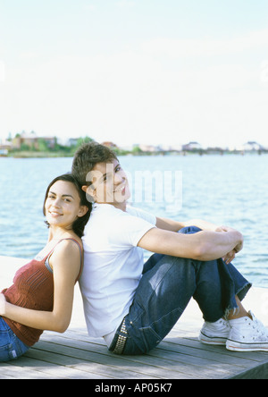 Junges Paar sitzen Rücken an Rücken auf dock Stockfoto