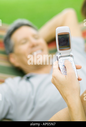 Hand unter Bild des Menschen in Hängematte mit Foto-Handy Stockfoto