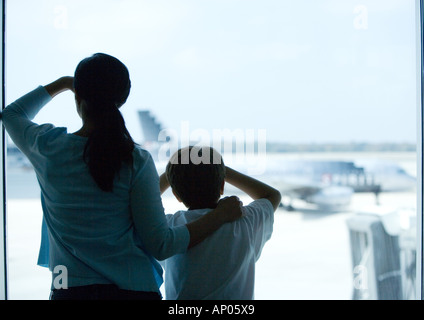 Frau und junge Blick durch Fenster im Flughafen Stockfoto