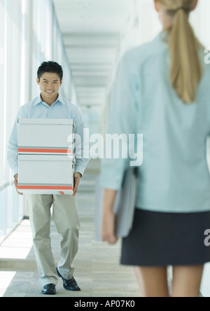 Mann trägt Kisten im Flur, Kollegin lächelte Stockfoto