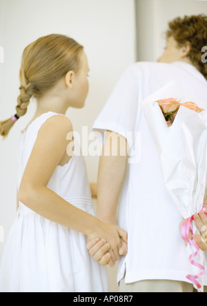 Kinder halten Strauß Rosen Rücken, schaut sich um Ecke Stockfoto