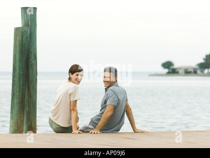 Paar sitzt am Rand des Hafenbeckens, über die Schultern in die Kamera Lächeln Stockfoto