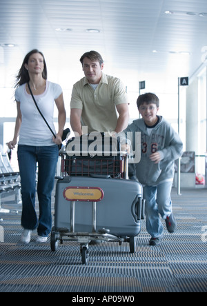 Familie eilen durch den Flughafen mit Gepäckwagen Stockfoto