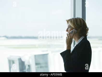 Frau mit Handy im Flughafen, Blick aus Fenster Stockfoto