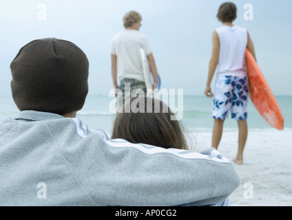 Paar am Strand mit Blick auf zwei Surfer Blick auf Wellen, Rückansicht Stockfoto