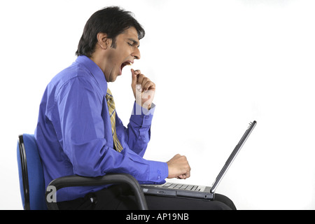 ANG200150 Executive ruht auf einem Stuhl mit Laptop auf dem Schoß müde und Gähnen Modell release Nr. 687 M Stockfoto