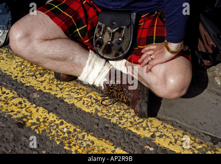 Ein schottischer Mann in einem Kilt sitzt neben der Straße Stockfoto