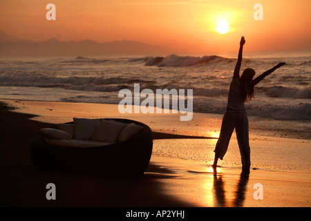 Eine junge Frau tut Übungen am Strand bei Sonnenuntergang, in der Nähe von Uluwatu, Bali, Indonesien Stockfoto