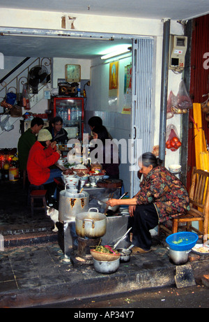 Ältere vietnamesische Frau, die vor ihrem Haus auf dem Bürgersteig in Hanoi, Vietnam, Essen kocht Stockfoto