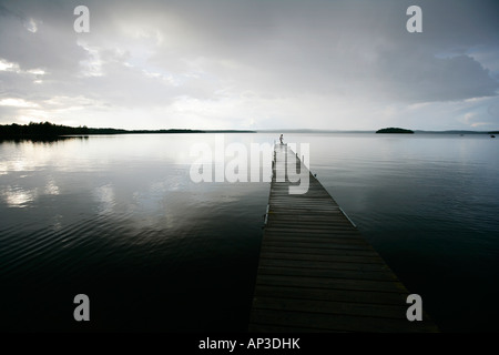 Eine Person steht am Ende ein Holzsteg am See an einem bewölkten Tag, Madkroken in der Nähe von Vaexjoe, Smaland, Schweden Stockfoto