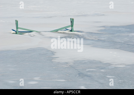 grüne Upside-down Park bench in gefrorenen Schnee und Eis auf Teich mit crack Stockfoto