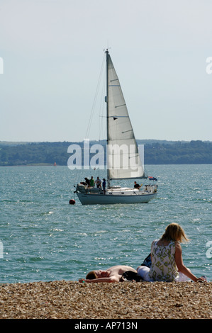 ein junges Paar den Hof saß sitzend liegend ein Kiesstrand mit einer Yacht in der Ferne und der Isle Of Wight jenseits solent Stockfoto