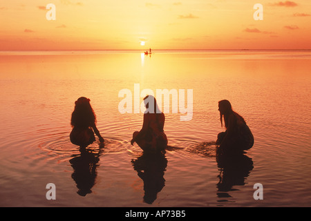 Drei junge polynesischen Frau in Insel Aitutaki Lagune bei Sonnenuntergang mit entfernten Ausleger Stockfoto