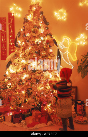 Junge Mädchen stehen neben dem hell beleuchteten Weihnachtsbaum zu Hause Stockfoto