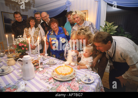 Die erste Geburtstagsparty mit drei Familiengenerationen lächelnd an Tisch mit Kerzen, Kaffee und Kuchen Stockfoto