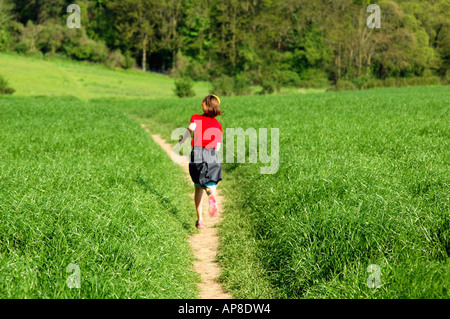 Junges Mädchen läuft durch ein grünes Feld auf dem Land an einem warmen Sommertag. Stockfoto