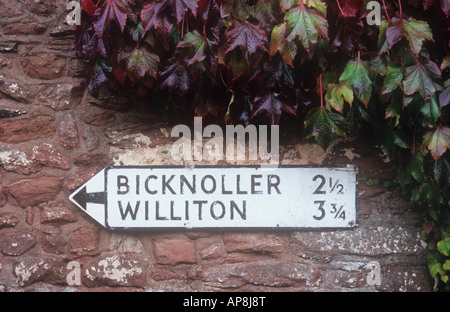 Altmodische schwarz-weiß Metall Schild auf rotem Sandsteinwand mit japanischen Ivy besagt Bicknoller 2 Williton 3 geschraubt Stockfoto