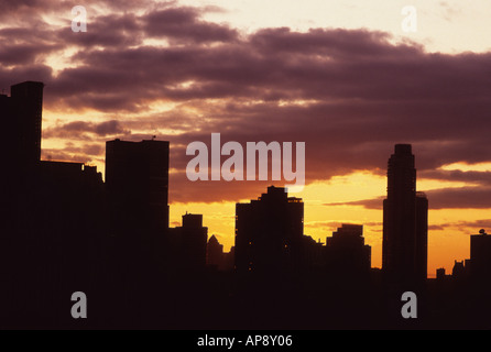 USA, New York City, Midtown Manhattan Towers. Die Gebäude wurden in der Dämmerung gegen eine untergehende Sonne silhouettiert. Dunkle Wolken am Himmel. Stockfoto