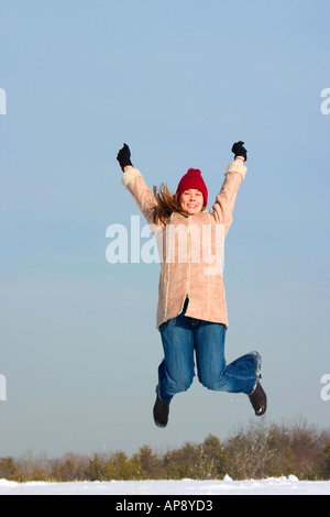 A pretty young woman jumps for joy on a sunny winter day. Stockfoto