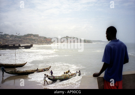 Junger Mann, Blick von der Stadtmauer von Cape Coast Castle auf Fischerboote auf den Strand Ghana ausgearbeitet wird Stockfoto