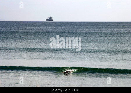 Surfer am Strand mit großen Schiff im Hintergrund heraus zum Meer Mt Manganui New Zealand Stockfoto