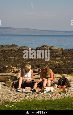 Zwei Frauen Touristen sitzen auf Log mit Hunden am Strand west Küste Schottlands Stockfoto