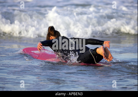 Surferin im Neoprenanzug Paddeln auf einem rosa Surfbrett in die Wellen aus weißen Felsen Strand portrush Stockfoto