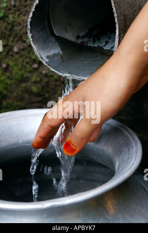 Eine Mädchen hält ihre Hand in den Strom des Wassers, während ihr Krug aus der Quelle, Kaschmir, Pakistan füllt Stockfoto