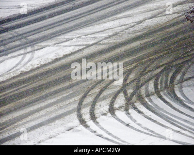 Gebogene und gerade Reifenspuren überschneiden sich in den frisch gefallenen Schnee. Stockfoto