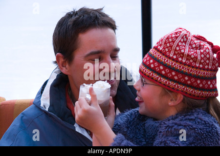 Vater und Tochter trinken heiße Schokolade neben eine Eislaufbahn. Stockfoto