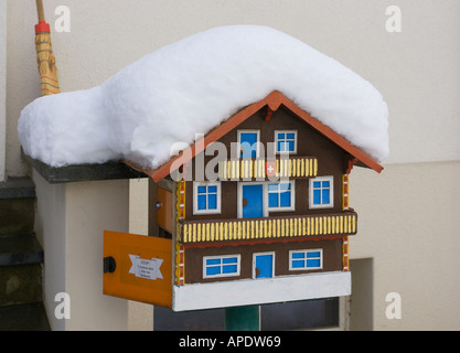 Haus Briefkasten gemacht wie eine kleine Miniatur bedeckt Swiss Chalet auf einem kurzen Mast vor einem lokalen Personen-Haus im Schnee Schweiz Stockfoto