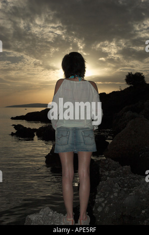 Junge Frau trägt Freizeitkleidung stehen auf Felsen vom Ozean genießen schöne Sonnenuntergang über Adria Rückansicht Stockfoto