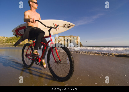 Ein Mann mit einem Surfbrett mit dem Cruiser-Fahrrad am Strand im Natural Bridges State Park in Santa Cruz in Kalifornien Stockfoto