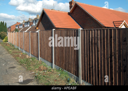 Wohnstraße mit neuen standard Holz Zaunverkleidungen Garten Grenze mit groben Rasen Rande Pflaster und Häuser Stockfoto