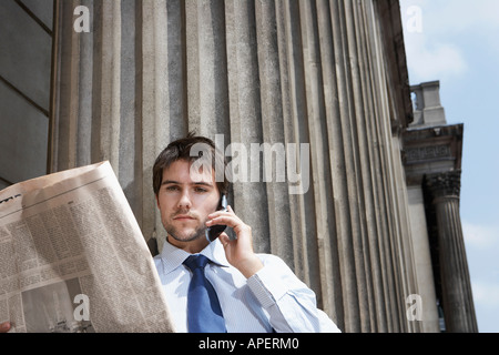 Geschäftsmann lesen Zeitung und Talking auf Handy außerhalb Gebäude Stockfoto